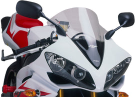 Clear PUIG racing windshield for motorcycle, aerodynamic windscreen with mounting hardware, designed for high-performance riding.