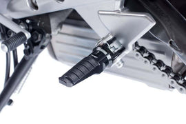 Black PUIG racing footpegs for motorcycle foot controls, with textured surface and mounting hardware visible.